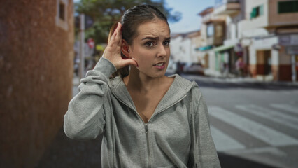 Fototapeta premium Woman cups ear with hand on city street crosswalk, straining to hear traffic and distant voices; confusion.