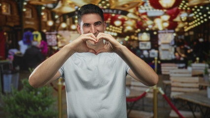 Fototapeta premium Man makes heart shape with hands at bustling street market with souvenir stalls; love community connection.