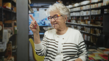 Obraz premium Elderly woman points finger to bookshelf in building, colorful glasses and red nails visible; gentle warmth.