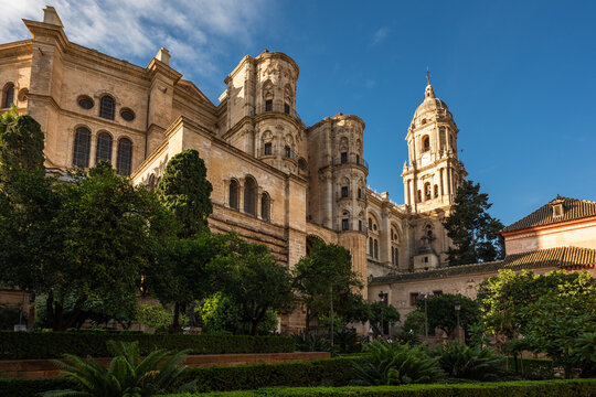Low angle perspective of the majestic facade and bell tower of the Malaga Cathedral (Catedral de la Encarnaci&oacute;n) under a partly cloudy sky, from a quiet square.