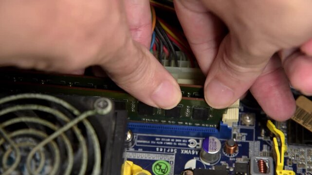 Close up of hand installing a RAM memory module into a computer motherboard slot