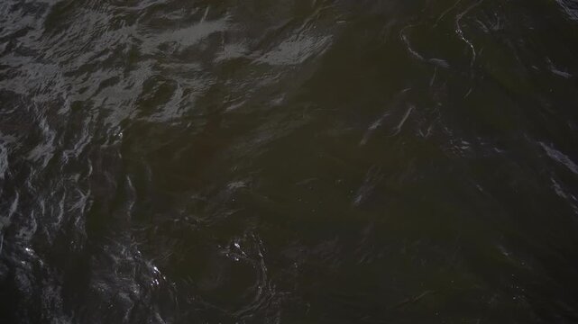 Dark river water current with sunlight reflection and liquid abstract pattern