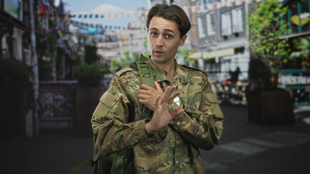 Man soldier in camouflage uniform touching dogtag and making ok sign with right hand while carrying backpack on street; duty resolve hope.
