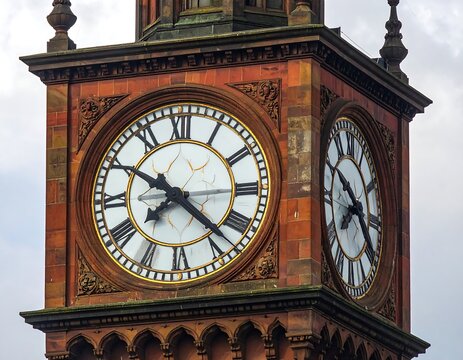 Close-up of ornate clock tower, red brick facade, two clock faces, Roman numerals, ornate carvings
