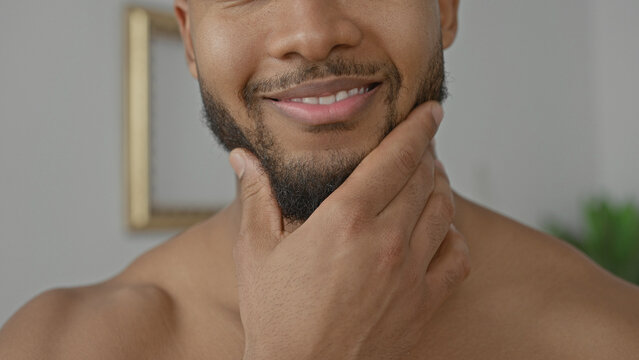 Man touching beard and chin with hand, shirtless in studio showing grooming gesture and gentle smile; confidence selfcare.