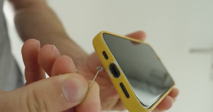 Close-up of a person removing lint and dust from a smartphone charging port, showing phone cleaning and device maintenance.