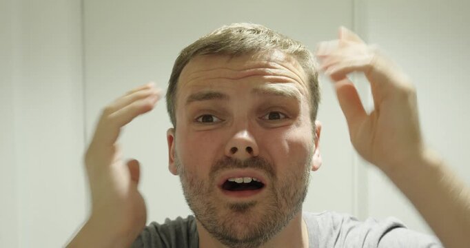 Man discovering his first gray hair and reacting with shock, showing aging concerns, surprise and personal appearance worries.