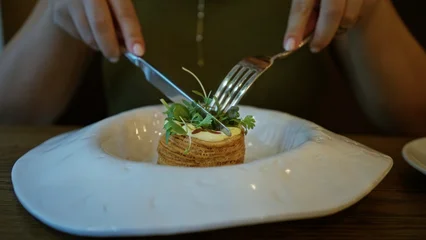 Woman cuts a layered pastry with knife and fork in building, close up on hands and plate  quiet mindful satisfaction. © Krakenimages.com