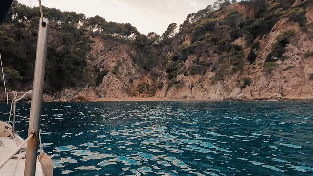 V&iacute;deo grabado desde una embarcaci&oacute;n frente a una cala rocosa, con agua azul en primer plano, acantilados mediterr&aacute;neos y vegetaci&oacute;n en la ladera. La escena transmite navegaci&oacute;n tranquila, naturaleza c