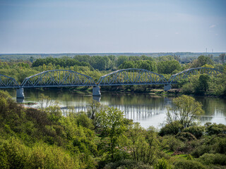 Fototapeta premium Steel railway bridge over river with surrounding green forest landscape