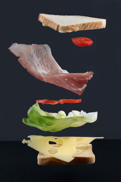 Between two slices of bread floating in the air, lettuce, cheese, and ham come together to form a sandwich.