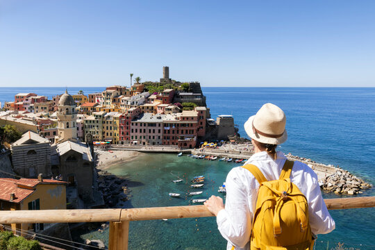 Tourism in Italy. Young female backpacker looking  the Cinque Terre National Park. Beautiful girl walks the Azure Trail and looking at Vernazza town, Italy.