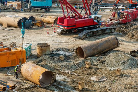 Large steel casing pipes, crawler crane and heavy machinery at active construction site in Busan, South Korea. Foundation engineering, deep piling operations and urban infrastructure development