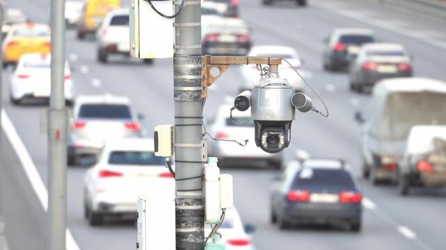 Dome-shaped traffic camera sits on a metal pole. Cars move steadily on a multi-lane city road. Active urban traffic monitoring. Perfect for security and transportation topics