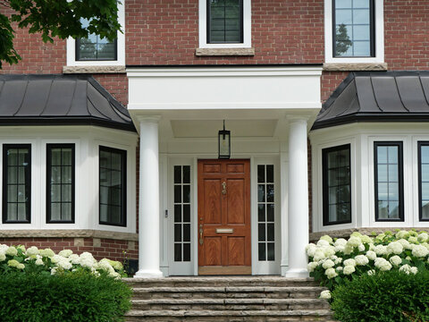 Traditional brick two story house with portico entrance and elegant wood grain front door