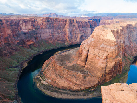 Aerial view of Horseshoe Bend with its iconic meander of the Colorado River carved into deep red sandstone cliffs under a cloudy sky in Page, Arizona, United States.