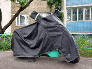 Black nylon motorcycle cover covering a motorbike parked in a quiet residential yard near an apartment building designed for weather resistance and outdoor storage safety © Harmony Video Pro