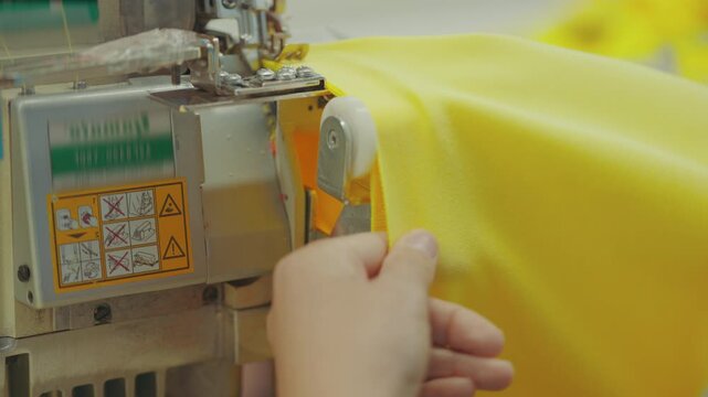 Detail shot of a garment worker using an industrial sewing machine to make a high-visibility vest.