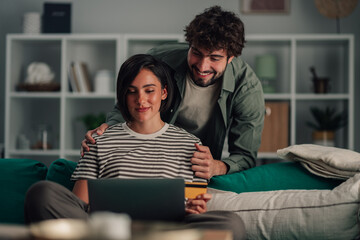 Couple relaxing at home, shopping online together with laptop and credit card, happy with secure e...