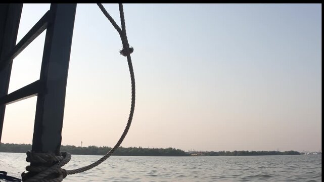 View from a ferry on the Chao Phraya River in Bangkok at dusk featuring a hanging rope and silhouette of the boat structure