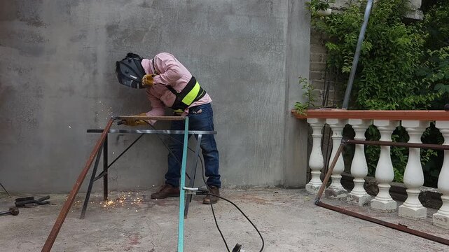 Young welder working next to a wall welding a metal profile