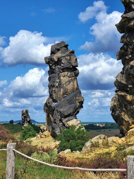 Imposante Sandsteinfelsen der Teufelsmauer im Harz. Eine markante Felsformation mit einer freistehenden Felsnadel vor blauem Sommerhimmel mit wei&szlig;en Wolken. Ideal als Naturbild.