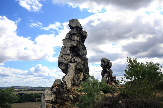 Imposante Sandsteinfelsen der Teufelsmauer im Harz. Eine markante Felsformation mit einer freistehenden Felsnadel vor blauem Sommerhimmel mit wei&szlig;en Wolken. Ideal als Naturbild.