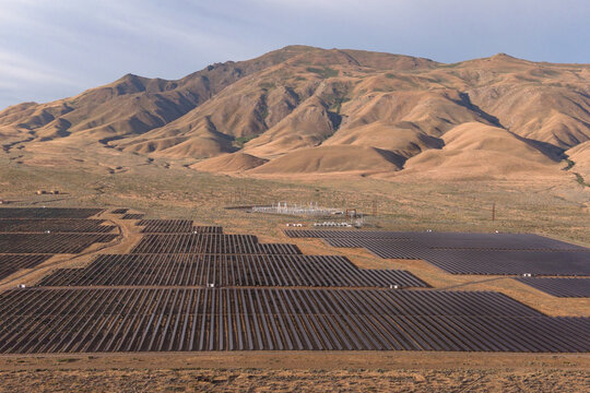 A utility-scale solar farm spreads across the northern Nevada high desert, with dramatic barren hills rising steeply in the background.