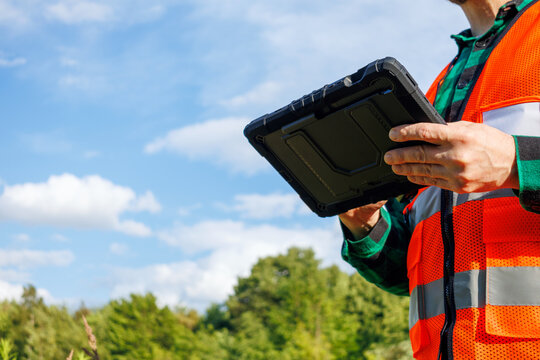 Close-up of an ecologist or meteorologist holding a rugged digital tablet while conducting outdoor research on climate change during a hot summer day. Environmental scientist or climatologist.
