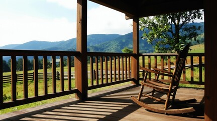 Fototapeta premium Wooden rocking chair on sunlit deck with mountain view. Greenery surrounds a peaceful porch, offering a tranquil outdoor seating space. Enjoy nature from this quiet retreat.