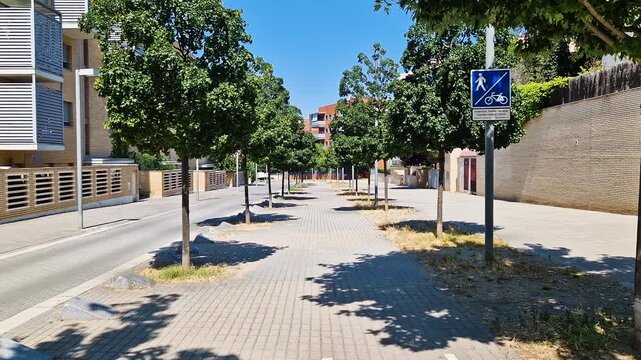 POV view of a sunny pedestrian path with rows of trees and a blue traffic sign in Spain