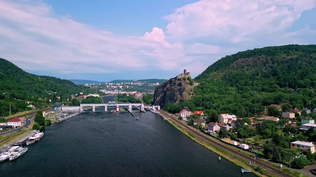 Aerial view of Strekov Castle overlooking the Elbe River, with lush green hills, residential buildings, and a bridge connecting both riverbanks in the Czech Republic