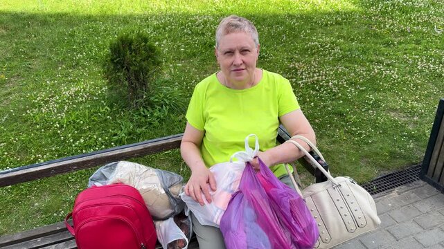 Woman sitting on bench with shopping bags outdoors. Woman in green shirt with multiple bags resting in park. Shopping, errands, outdoor break, summer day