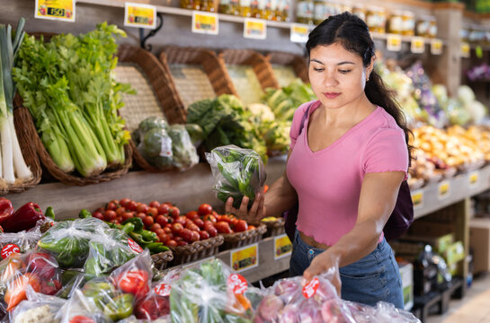 Adult female customer examines pre-packed vegetables in plastic bags at grocery store