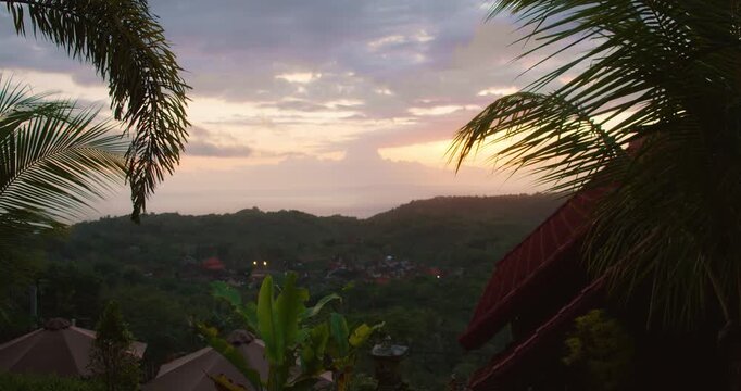 Tropical sunset over green dark hills framed by palm trees in Nusa Penida Bali