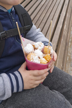 Child holding a paper cone with fried dough balls