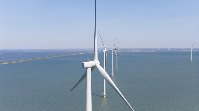Aerial view of Windpark Fryslan wind turbines standing in the water of the IJsselmeer, with a dike visible in the background in Breezanddijk, Friesland, Netherlands.