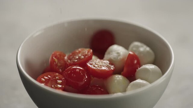 Slow motion making salad with mozzarella and cherry tomatoes, caprese style in white bowl closeup