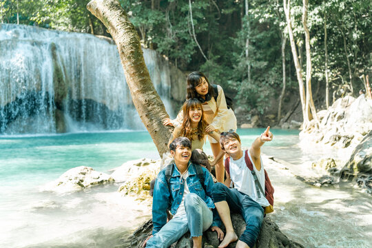Young Asian man and woman friends relaxing together by waterfall lagoon at tropical forest enjoying eco tourism adventure outdoor travel active lifestyle nature therapy on summer holiday vacation.