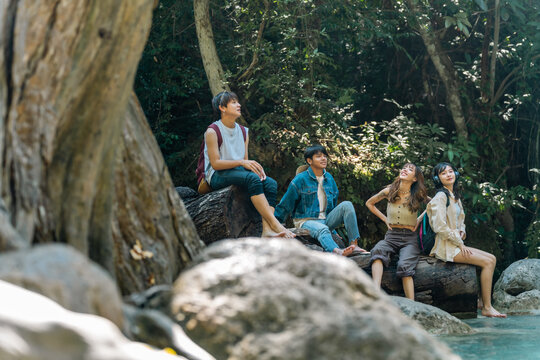 Young Asian man and woman friends relaxing together by waterfall lagoon at tropical forest enjoying eco tourism adventure outdoor travel active lifestyle nature therapy on summer holiday vacation.