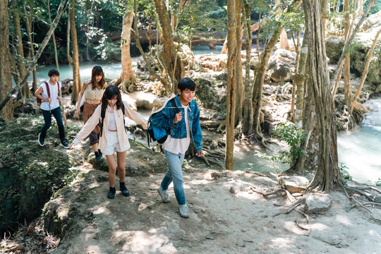 Group of Young Asian man and woman friends hiking through tropical forest trail together enjoying eco tourism adventure outdoor travel active lifestyle nature therapy on summer holiday vacation.
