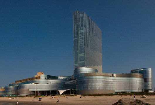 Ocean Casino Resort in Atlantic City, New Jersey with modern glass fa&ccedil;ade rising above a sandy beach, people strolling on the shore and urban skyline creating a dramatic coastal architecture