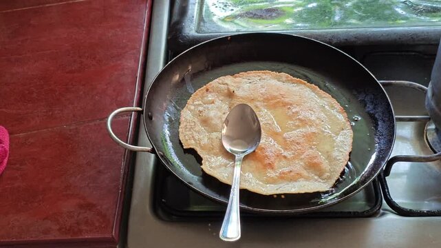 Spoon pressing corn tortilla frying in hot oil inside pan