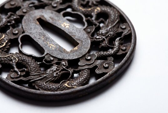 An ornate circular iron tsuba sword guard featuring intricate dragon motifs and metallic detailing.