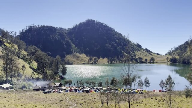 Ranu Kumbolo lake camping site with many colorful tents under green hills on Mount Semeru East Java Indonesia