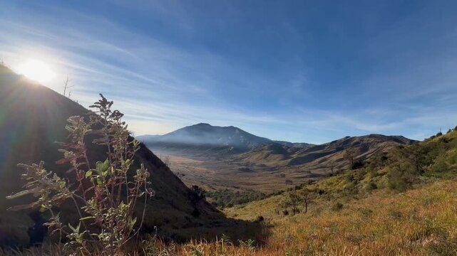 Scenic mountain valley landscape during sunrise with clear blue sky and bright sun flare