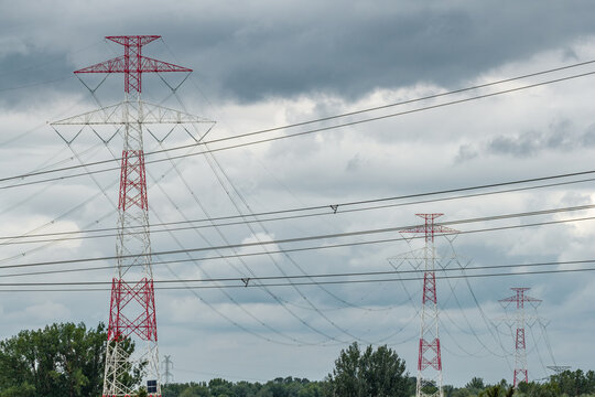 Aerial view of high-voltage power transmission towers with red and white lattice structures set against a cloudy sky in Poland.