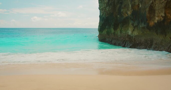 Tropical beach with blue ocean waves and limestone cliffs at Kelingking Beach Bali