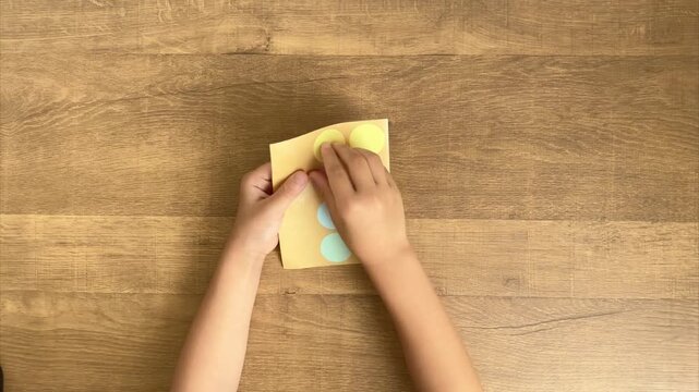 Child Peels a Yellow Round Sticker from a Sheet of Colorful Stickers, 4K