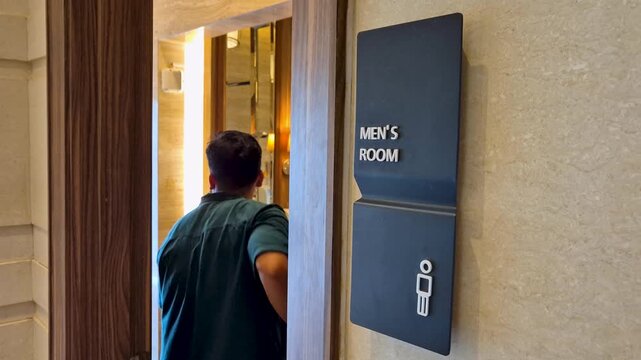 Modern black men's room sign with male icon on beige stone wall next to a wooden door frame